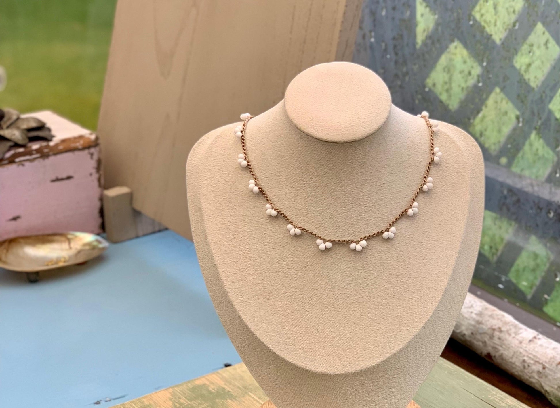 May include: A latte colored  crocheted chain necklace with white beads. The necklace is displayed on a white mannequin bust.